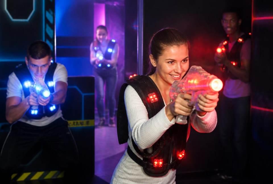 Quatre joueurs équipés de gilets lumineux visant avec leurs blasters derrière un obstacle de l'arène