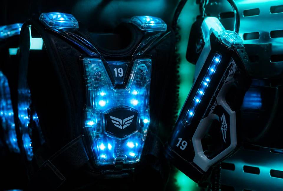 Gros plan sur un gilet de laser tag et un blaster aux LED bleues allumées