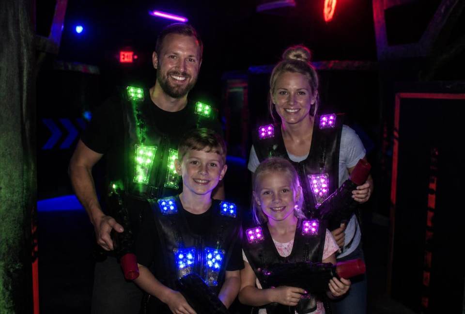 Parents et enfants équipés de gilets lumineux jouant ensemble dans l'arène de laser tag
