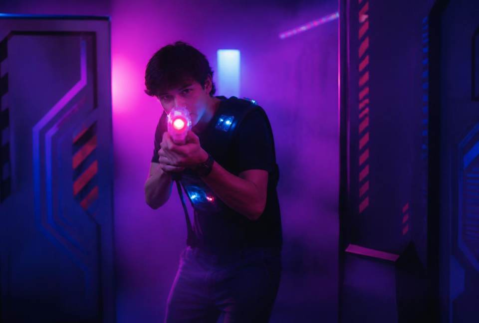 Joueur seul visant avec son blaster au milieu de l'arène éclairée de néons violets